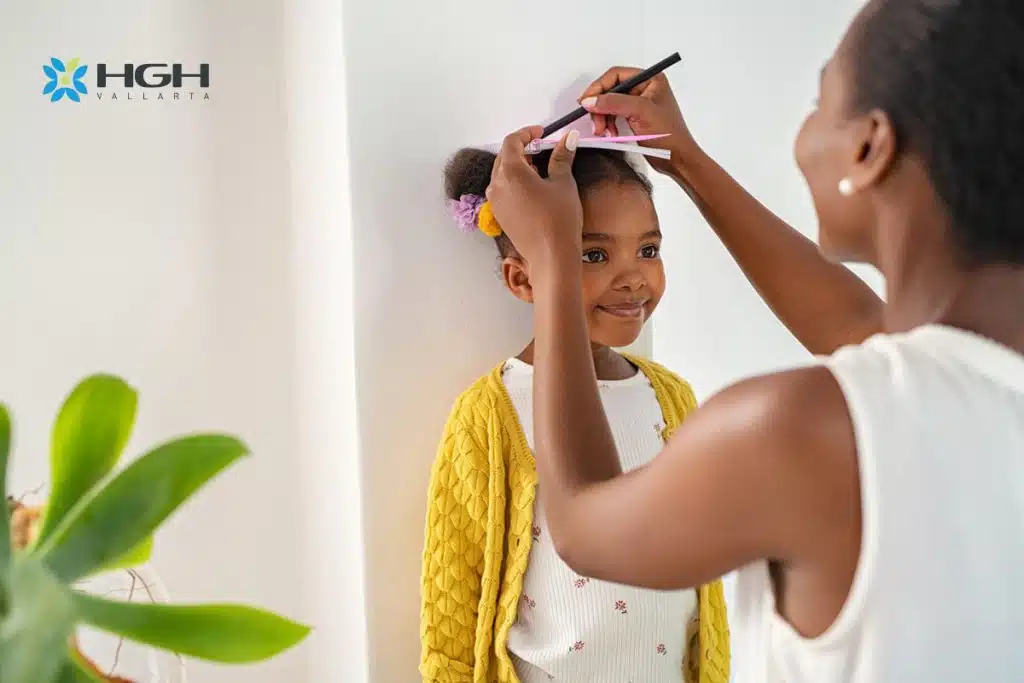 Black mother in white shirt measuring black daughter height against wall to determine if HGH for kids is right for her daughter