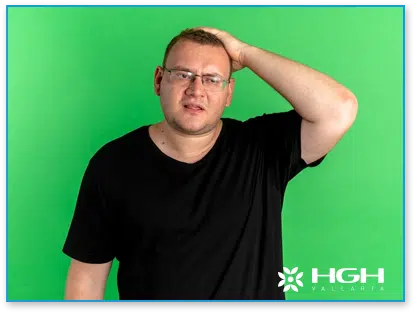 Man in black shirt touching hair with green background behind him to represent HGH dosage needed for hair growth